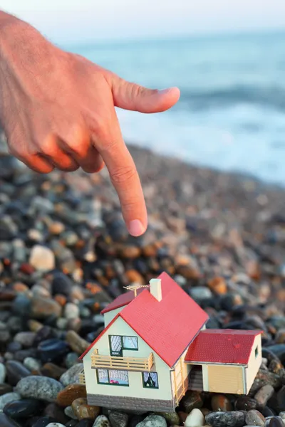 Μοντέλο του σπιτιού με γκαράζ στην πετρώδη παραλία βράδυ, το χέρι του ανθρώπου — Φωτογραφία Αρχείου