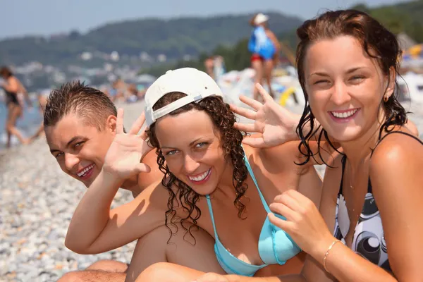 Hombre sonriente y dos mujeres jóvenes en la playa pedregosa —  Fotos de Stock