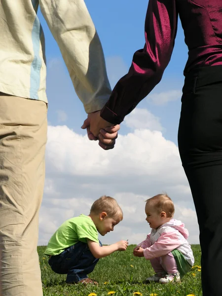 Děti sedí na trávě a matka s otcem drží ruce c — Stock fotografie