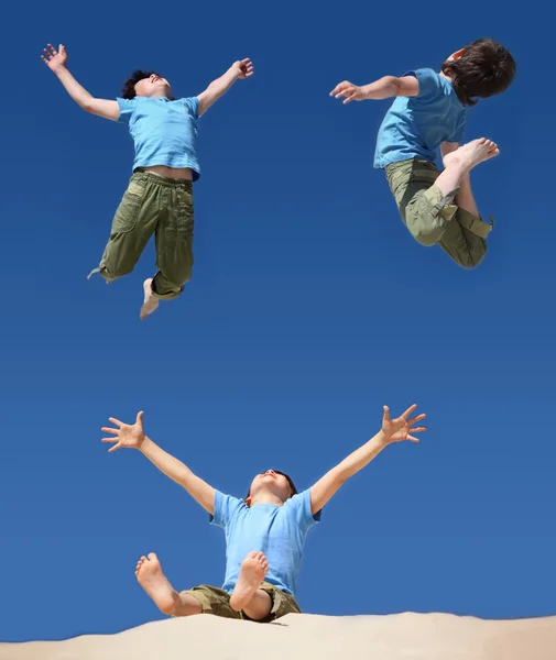 Saltando meninos no céu azul, menino sentado com as mãos e pernas para cima — Fotografia de Stock