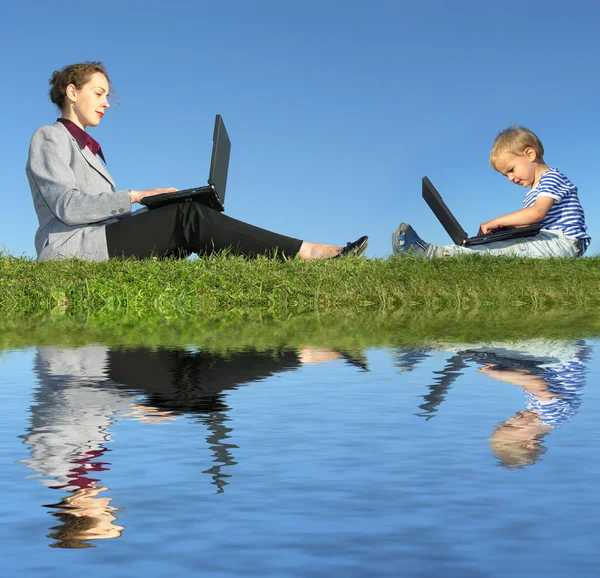Zakenvrouw en kind zitten met laptops op blauwe hemel, reflecti — Stockfoto