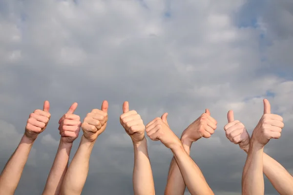 Hands with the raised thumbs against the background of the cloud sky — Stock Photo, Image