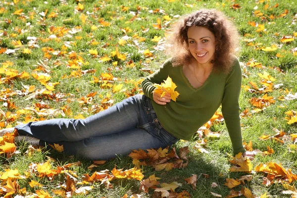 黄色の葉を持つ女性は草の上に座っています。 — ストック写真