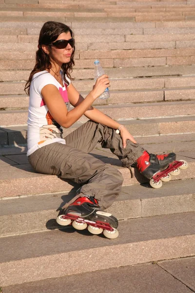 Девушка-каток сидит на лестнице с бутылкой воды — стоковое фото