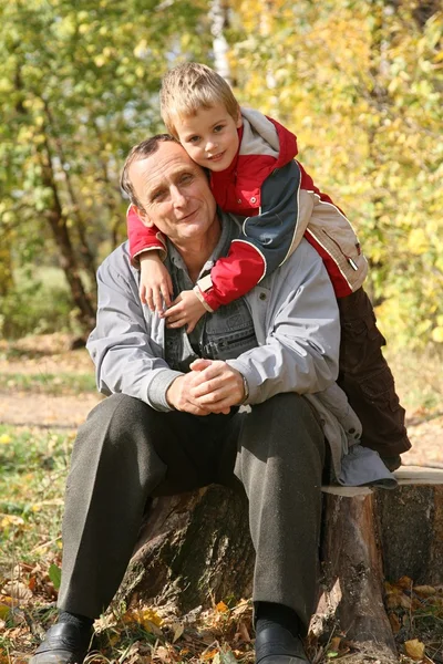 Grandfather with the grandson sit in park in autumn — Stock Photo, Image