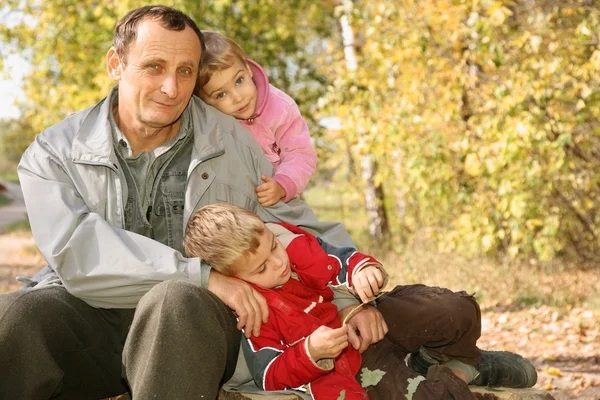 Grandfather with the grandson and the granddaughter in the park in autumn — Stock Photo, Image