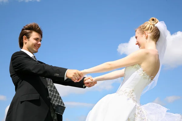 Невеста держит жениха за руки на фоне неба — стоковое фото