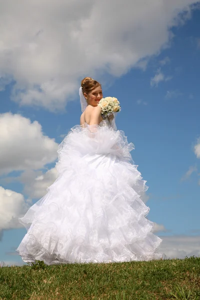 Nevěsta stojí s kyticí na louce na pozadí sk — Stock fotografie