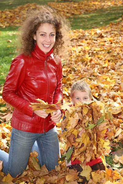 Moeder en kind onder gevallen bladeren — Stockfoto