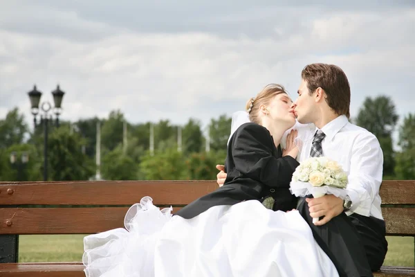 Noivo e noiva beijo no banco — Fotografia de Stock
