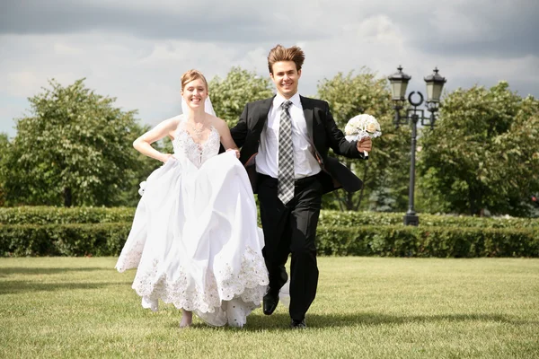 Невеста с женихом, которого они бегают по лужайке — стоковое фото