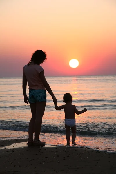 Mama z dzieckiem na zachód słońca na morzu — Zdjęcie stockowe