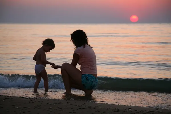 Mamá con el niño en la orilla del mar al atardecer — Foto de Stock