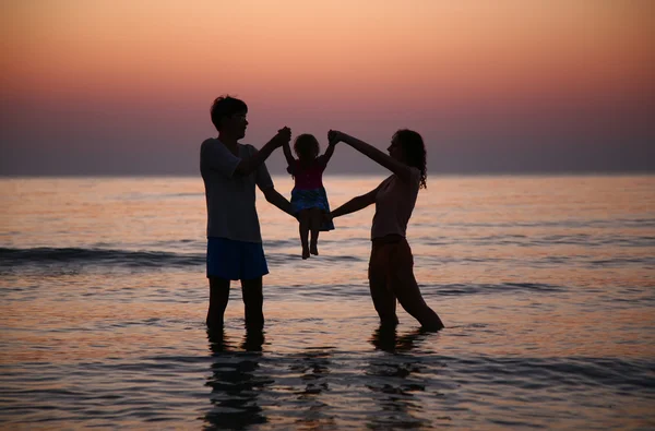 Anne ve baba gün batımında çocuğu denizde tutuyor. — Stok fotoğraf