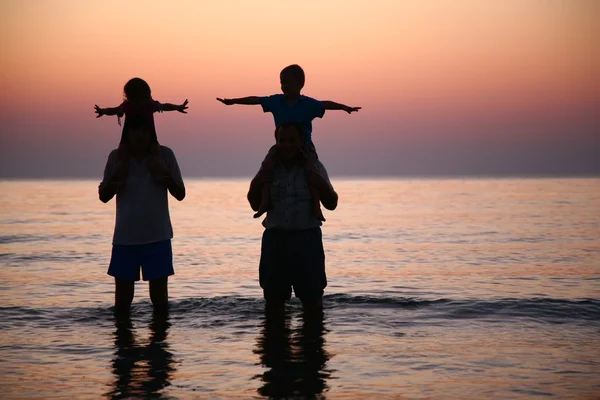 Два человека в море с детьми на плечах — стоковое фото