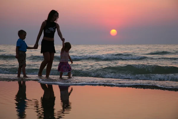 Мать с детьми на берегу на закате — стоковое фото