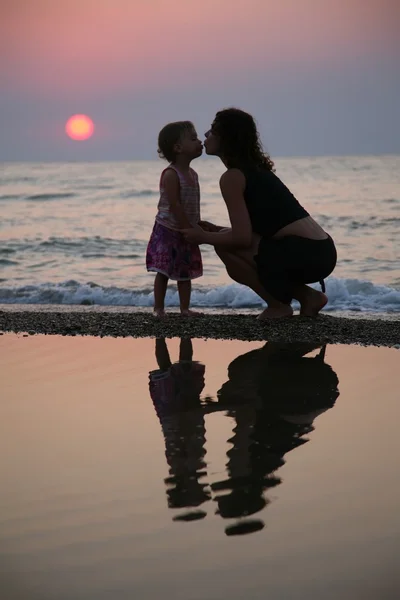 Mamma med dotter iland på sunset — Stockfoto