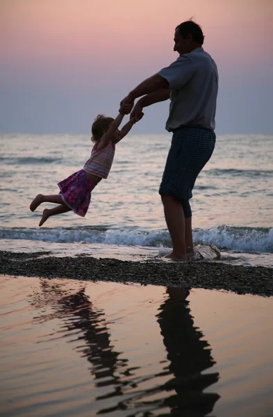 Grandfather rotates child on sunset at sea — Stock Photo, Image