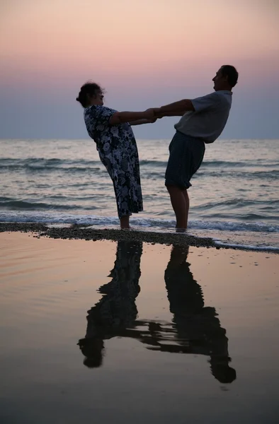 O avô mantém a avó de mãos no pôr do sol no mar — Fotografia de Stock