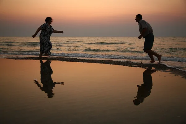 Дедушка с бабушкой на закате у моря бегают — стоковое фото