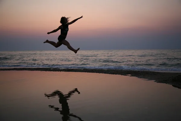 Νεαρή γυναίκα άλματα στην παραλία στο ηλιοβασίλεμα — Φωτογραφία Αρχείου