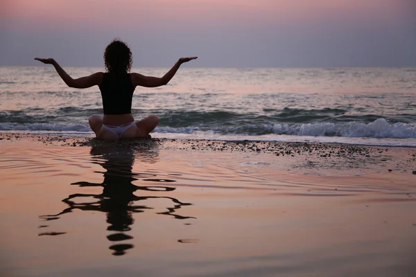 Ung kvinna platser på stranden vid solnedgången — Stockfoto