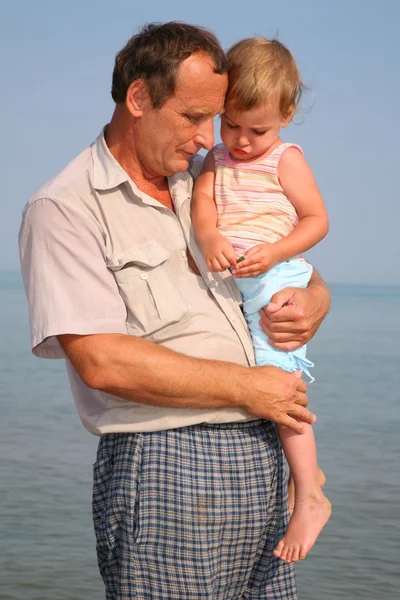 Дедушка держит внучку на руках в море — стоковое фото