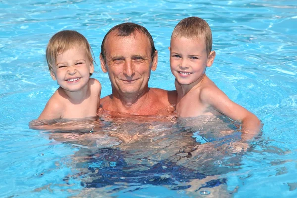 Grootvader houdt kleinzonen op handen in zwembad — Stockfoto