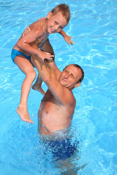 Дедушка держит внука на руках в бассейне — стоковое фото