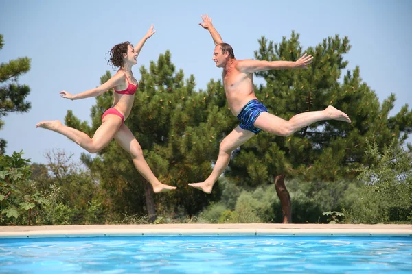 Woman and man jump over pool — Stock Photo, Image