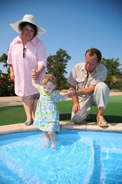 祖父、 祖母举行孙女在游泳池中 — 图库照片