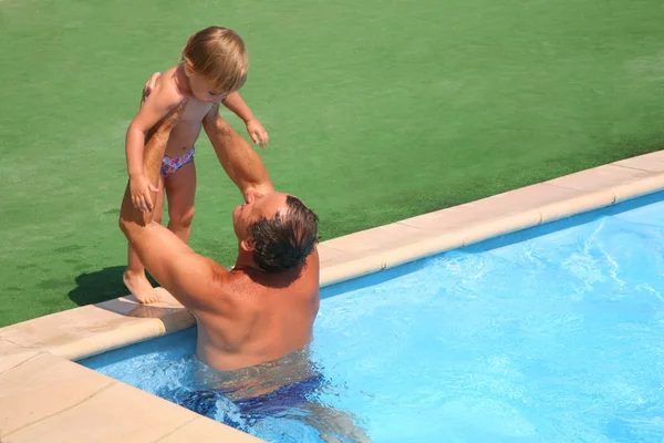 Grandfather standing in pool holds on hands granddaughter — Stock Photo, Image