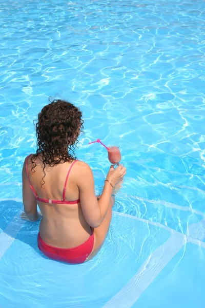 A mulher com uma bebida senta-se na piscina — Fotografia de Stock