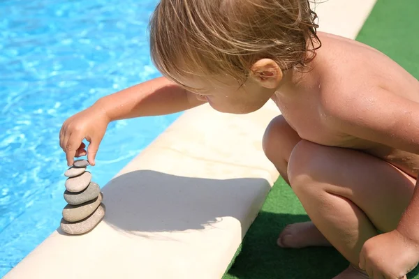 El niño construye una figura de piedras alrededor del agua —  Fotos de Stock