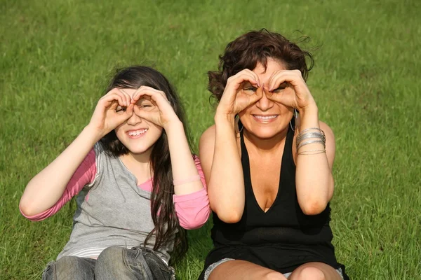 Mother and daughter sit on the grass and look forward — Stock Photo, Image