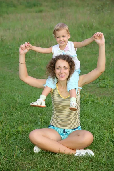 Hija se sienta sobre los hombros en la madre en el prado —  Fotos de Stock