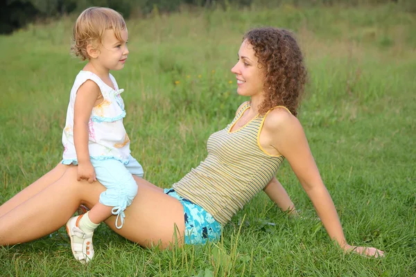 Daughter seats on knees at mother on to the meadow — Stock Photo, Image