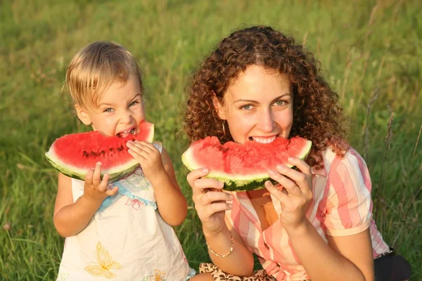 Anya és lánya enni görögdinnye a fűben — Stock Fotó