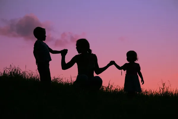 Mãe segura crianças para as mãos no pôr do sol — Fotografia de Stock