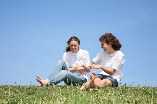 Duas amigas em T-shorts brancos têm um resto em uma grama — Fotografia de Stock