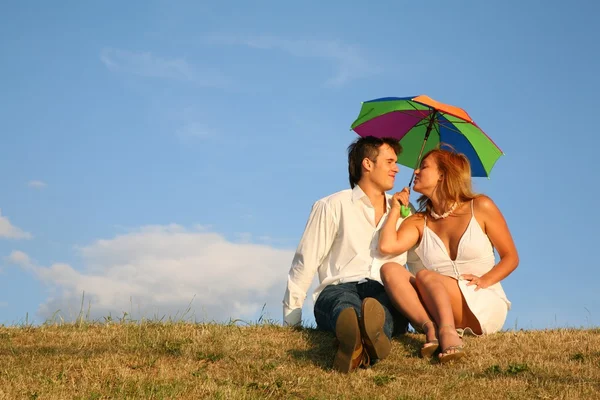 Casal sentar-se no prado sob guarda-chuva — Fotografia de Stock