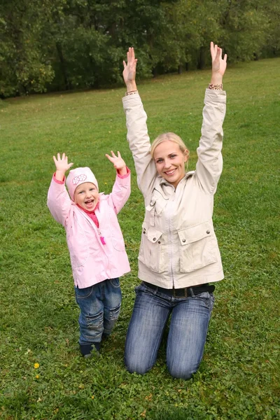 Mor och dotter sitta på gräset och höjde händerna uppåt — Stockfoto