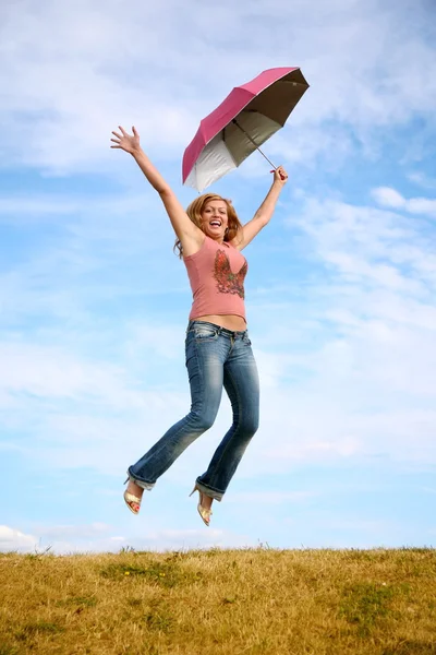 Ung kvinna hoppar med paraply på ängen — Stockfoto