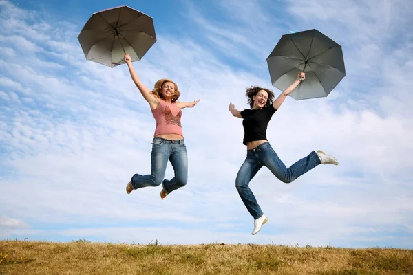 Two young women jump with the umbrellas — Stok fotoğraf