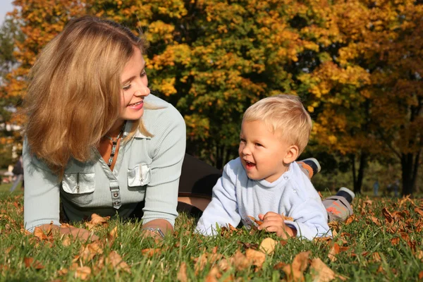 Mother and son lie on the grass at the park in autumn — Stock Photo, Image