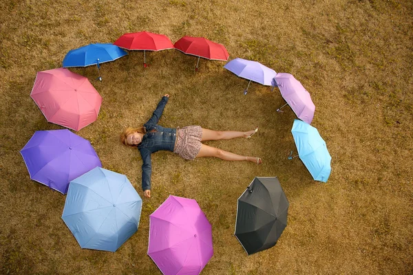 Junge Frau liegt im Gras am Ring von den Regenschirmen — Stockfoto