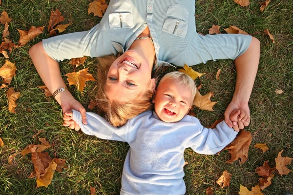 Blauäugiger Blondschopf liegt mit Sohn im Herbst im Park auf der Erde — Stockfoto