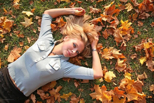 Blauäugige Blondine liegt zwischen gelben Blättern 3 — Stockfoto