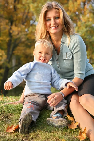 Loira de olhos azuis senta-se com o filho no parque no outono — Fotografia de Stock