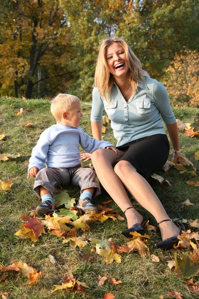Blue-eyed blond sits with the son in the park in autumn 2 — Stock Photo, Image
